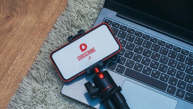 A laptop, phone and phone tripod with a YouTube subscribe button on it